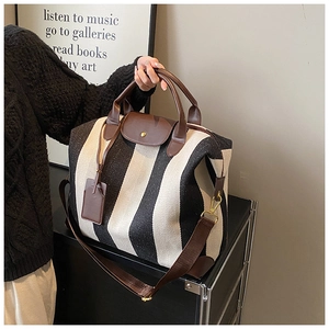 Détail d'un grand sac de voyage rayé avec poignées en cuir et bandoulière marron réglable