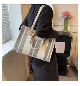 Detailed view of striped canvas tote bag with leather trim worn over the shoulder