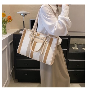 Detail of striped contrast tote bag with leather strap and metal buckle on the model