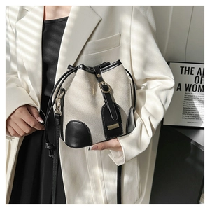 Detail of a bucket bag with beige canvas and black leather trim with drawstring closure