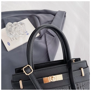 Detail of black faux crocodile leather bag showing golden twist lock and textured finish