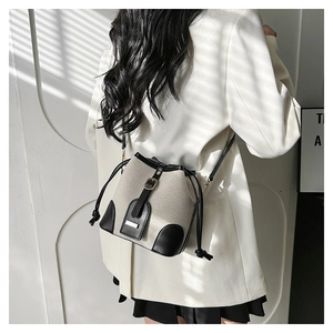 Detail of canvas bucket bag with black leather trim and drawstring worn by model