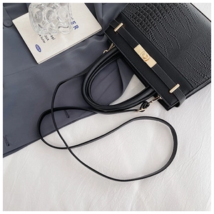 Detail of black crocodile texture handbag featuring golden twist lock and thin shoulder strap