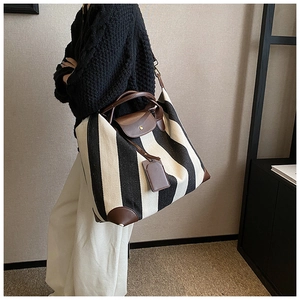 Détail du sac cabas en toile rayée avec poignées en cuir marron et coutures soignées