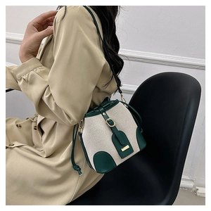 Detail of canvas bucket bag with green leather trim worn with khaki trench coat