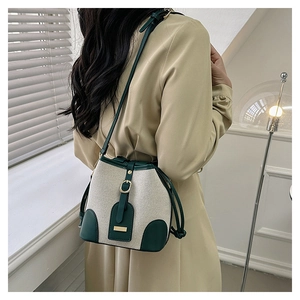 Detail of canvas bucket bag with green leather trim and golden buckle on a model