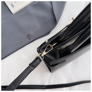 Close-up of black litchi grain leather texture and gold hardware on a square handbag