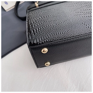 Detail of black faux leather bag showing crocodile texture and gold protective metal feet