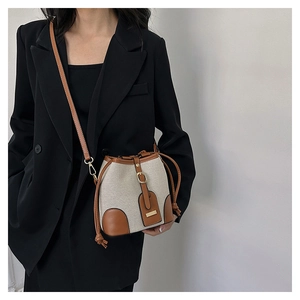 Detail shot of a canvas bucket bag with brown leather trim worn by a model