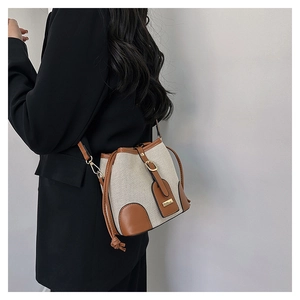 Detail of canvas bucket bag with brown leather trim and gold hardware on a model