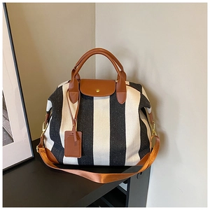 Détail du grand sac de voyage en toile rayée avec poignées en cuir brun et métal doré