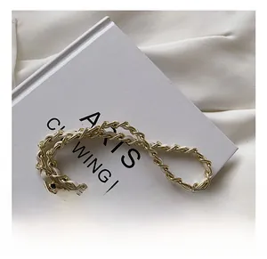 Detail of gold metal and white leather woven chain strap with decorative gold ball