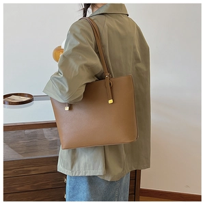 Sac fourre-tout en cuir marron avec texture grainée et boucle dorée porté à l'épaule du modèle