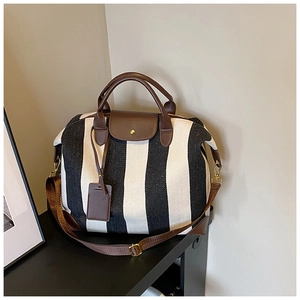 Détail du sac de voyage rayé noir et blanc avec anses en cuir et crochets dorés