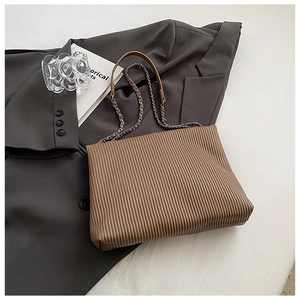 Detail of a brown pleated shoulder bag with a silver chain strap on a grey suit jacket