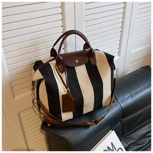 Détail du sac de voyage en toile rayée avec finitions en cuir brun sur canapé noir