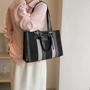 Large striped canvas tote bag with black leather trim shown on a female model