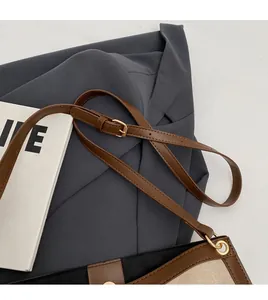 Detail of adjustable leather shoulder strap with golden metal buckle on a canvas bucket bag