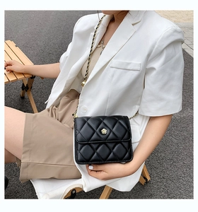 Detail of black quilted leather crossbody bag with golden camellia flower buckle ornament
