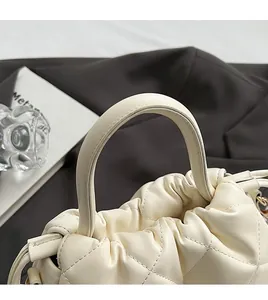 Detail view of the elegant arched handle and quilted diamond pattern on beige bucket bag