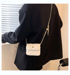 Detail of white quilted crossbody bag with golden flower clasp and chain strap