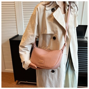 Pink crescent shoulder bag with vertical pleats worn over a beige trench coat