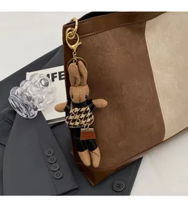 Detail of a brown knitted rabbit keychain with houndstooth vest on a bucket bag