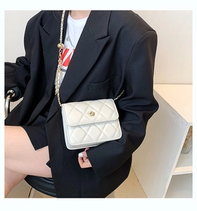 Detail of white quilted crossbody bag with golden floral clasp and metal chain strap