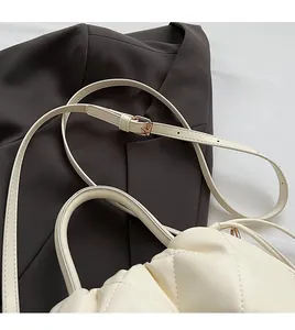 Detail of cream quilted bag showing adjustable thin strap with pale gold metal buckle