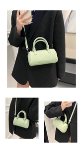 Detail view of a pale green pleated cylinder handbag with silver ring handles and shoulder strap