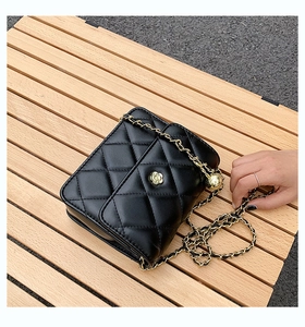 Detail of black quilted leather crossbody bag featuring gold chain and camellia floral clasp