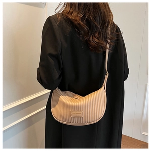Detail view of beige pleated crescent bag with adjustable strap worn on black coat
