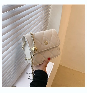 Detail of white quilted handbag featuring a golden camellia clasp and chain strap
