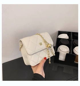 Detail of white quilted crossbody bag featuring a golden rose clasp and chain strap