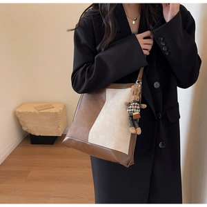 Detail of a large color-block tote bag with a cute bear pendant on a model in a black blazer