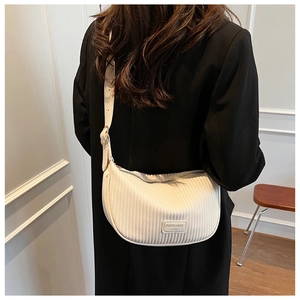 Detail of pleated beige half-moon bag with adjustable strap worn on a black blazer