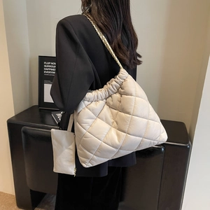 Detail of cream quilted tote bag featuring metal chain strap and pleated design