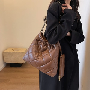 Detail of brown quilted tote bag with chain strap and matching small pouch on a model