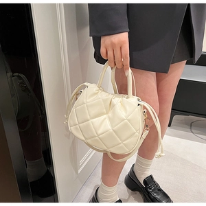 Close-up of cream quilted bucket bag with drawstring detail and metal shoulder strap hardware