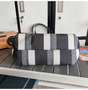 Detail of a large striped canvas tote bag with black leather handles on a metal table