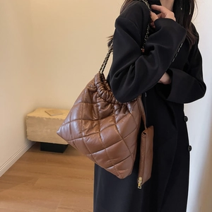 Detail of brown quilted tote bag with drawstring closure and metal chain strap