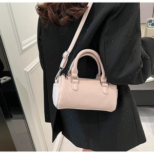 Close-up of pink pleated cylinder bag worn crossbody over a black beaded suit jacket