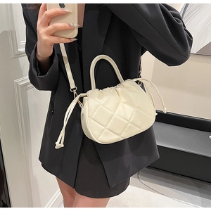 Detail of cream quilted crossbody bag with drawstring side and round handle on a model