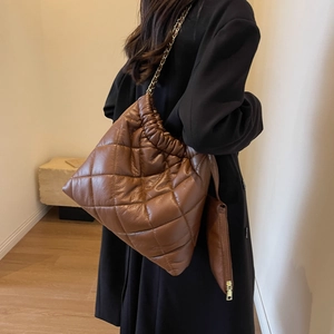 Detail of brown quilted tote bag with drawstring closure and metal chain strap