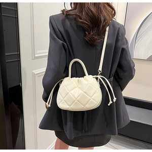 Detailed view of beige quilted bucket bag styled with a professional black blazer