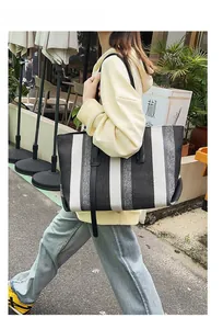 Street view of a large striped canvas tote bag with black leather handles on a model