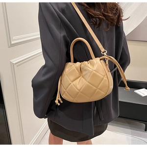 Detail of light brown quilted bucket bag with drawstring closure and crossbody strap