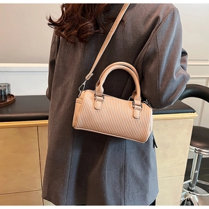 Detail of apricot Boston bag with pleated texture on a model wearing a grey blazer