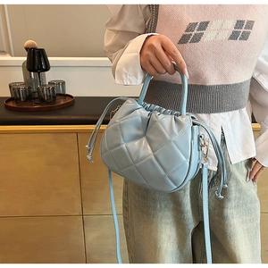 Detail of light blue quilted bucket bag with drawstring closure and golden hardware