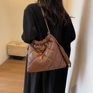 Detail view of a quilted brown tote bag with leather chain strap on a model wearing black